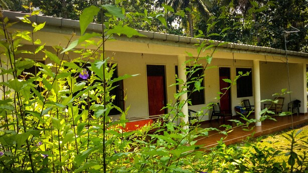 Un edificio con varias habitaciones, un porche cubierto y un jardín con diversas plantas y flores.
