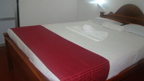 Una cama bien tendida con una colcha roja y sábanas blancas, un cabecero de madera y una lámpara fijada a la pared.