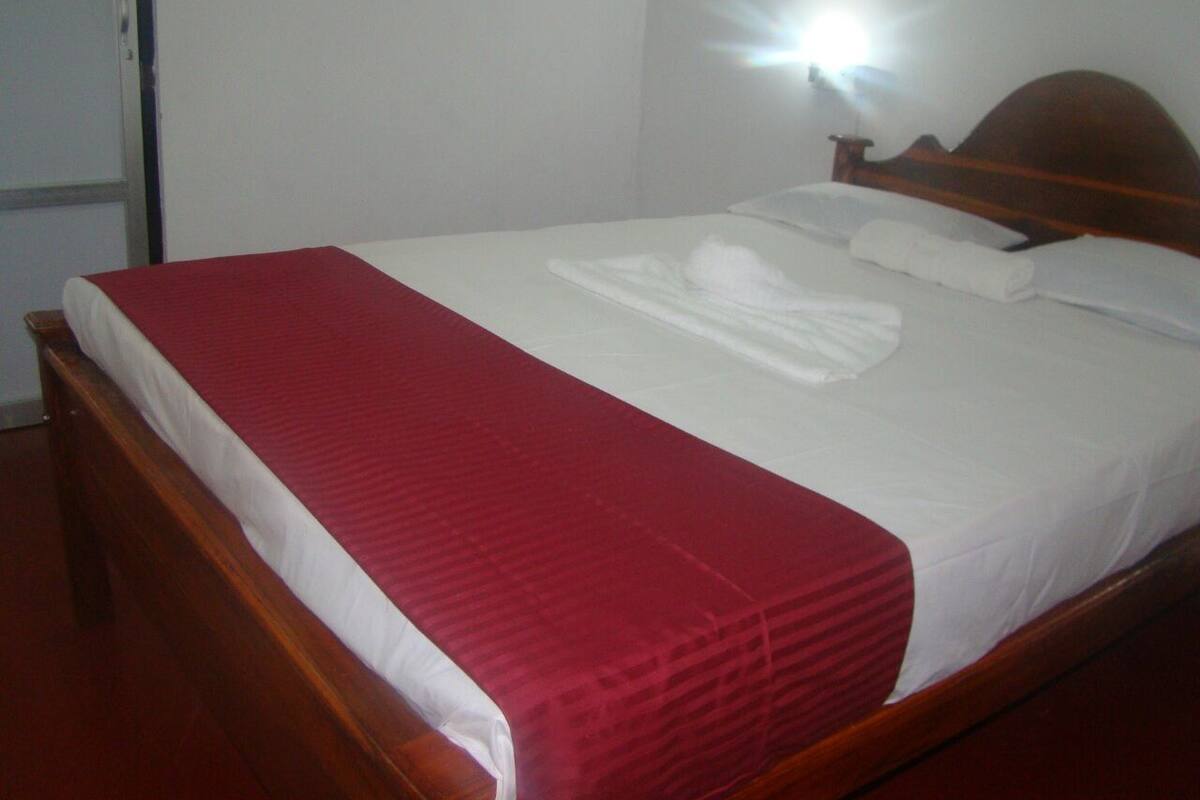 A neatly made bed with a red blanket and white sheets, a wooden headboard, and a wall-mounted light.