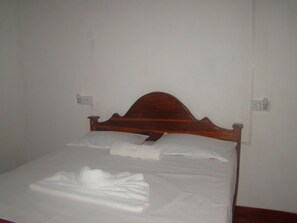 Un letto singolo con una testiera in legno, lenzuola bianche e un asciugamano piegato sul letto.