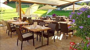 Un restaurant en plein air avec des tables et des chaises, des parasols et une vue sur un terrain de golf.