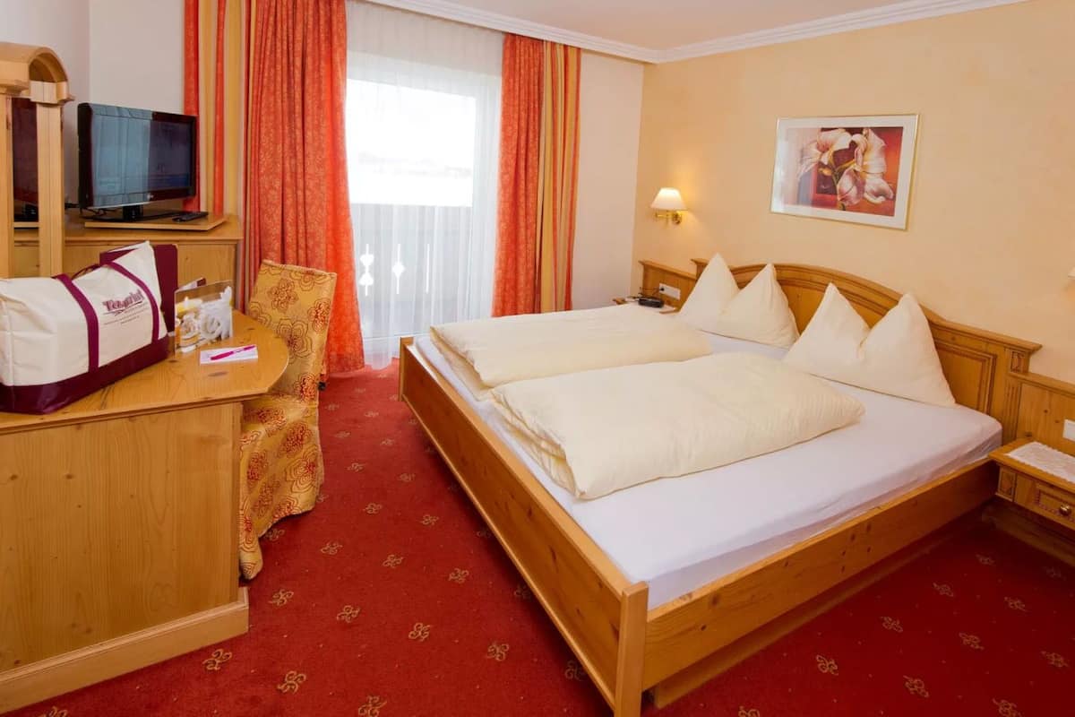 Une chambre d’hôtel avec un lit en bois, un bureau avec une télévision, une chaise et une moquette rouge.