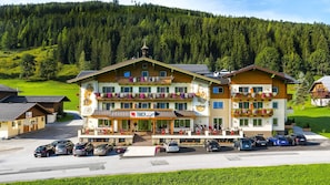 A hotel with a central entrance, multiple balconies with flower boxes, and a parking lot. - Hotel Taxerhof (Radstadt)