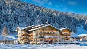 Un hôtel à plusieurs étages, de style architectural alpin traditionnel, doté de balcons et d’une entrée imposante.