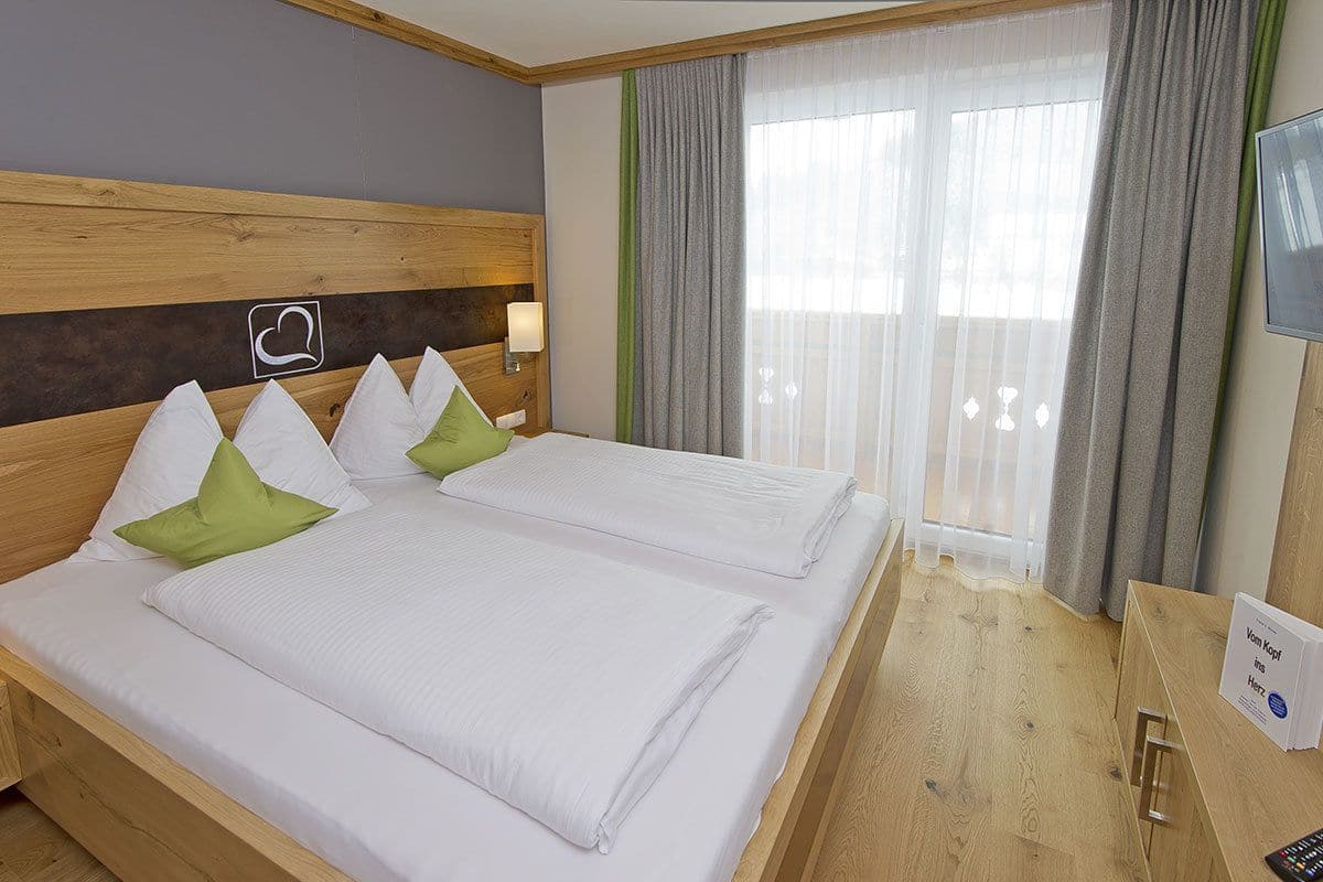 Un lit double avec des oreillers blancs et verts, une tête de lit en bois, une table de chevet avec une lampe et un téléviseur fixé au mur.