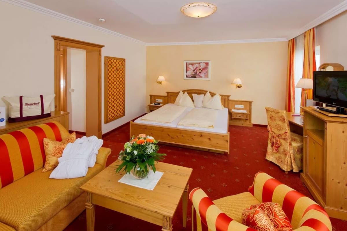 Une chambre d’hôtel avec un lit, deux canapés, une télévision et une table ornée d’un vase de fleurs.