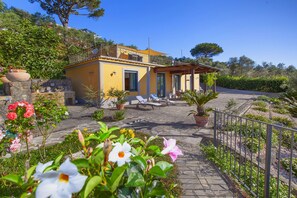Une villa jaune dotée d’un patio, d’un espace salon extérieur et d’un jardin fleuri.