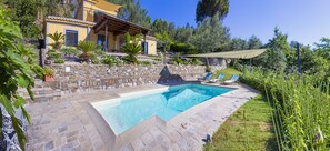 Un espace piscine doté d’une terrasse en pierre, de chaises longues et d’un bâtiment jaune avec un balcon.