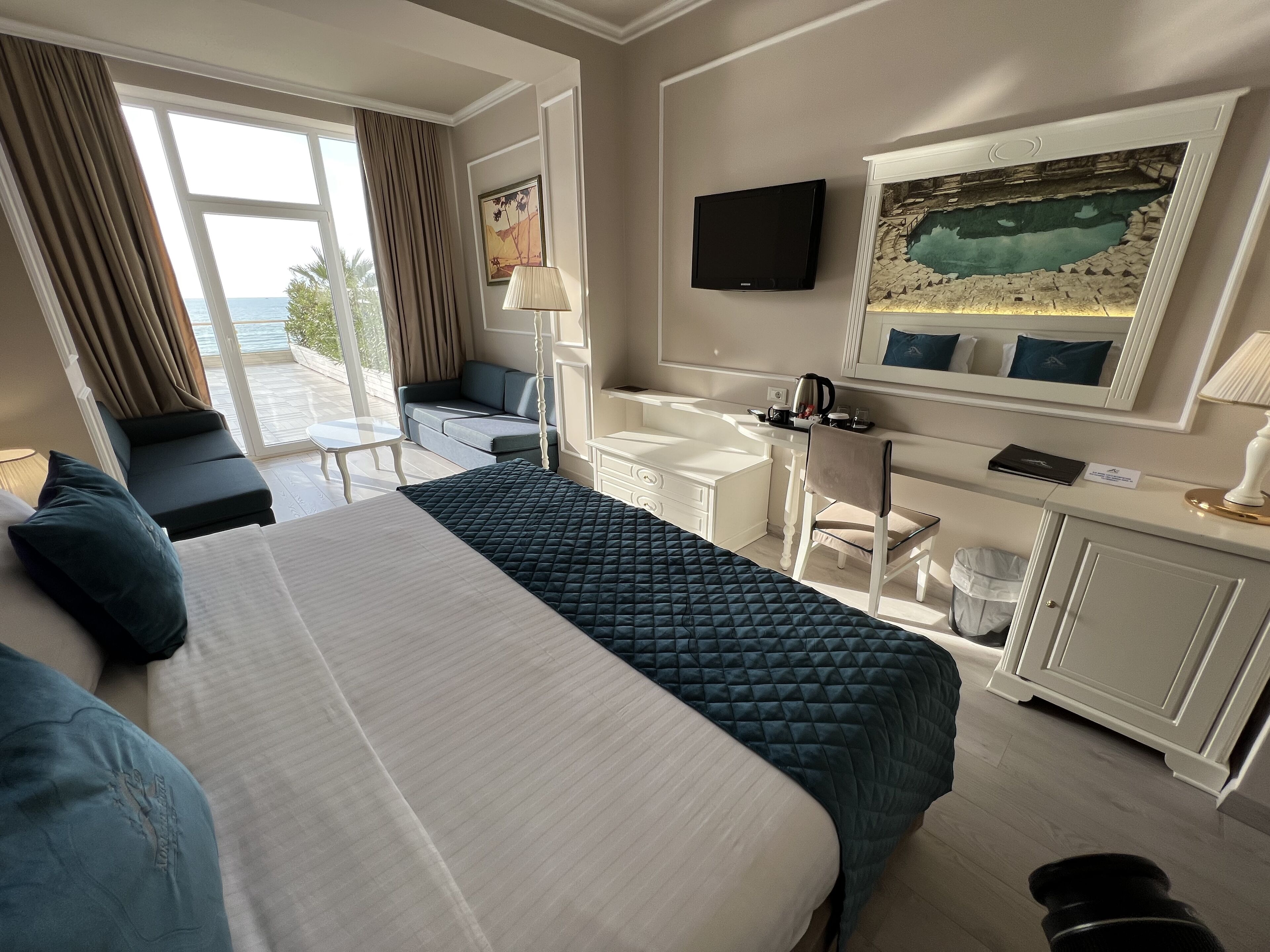 Een hotelkamer met een bed, een bureau, een stoel, een televisie en uitzicht op zee.