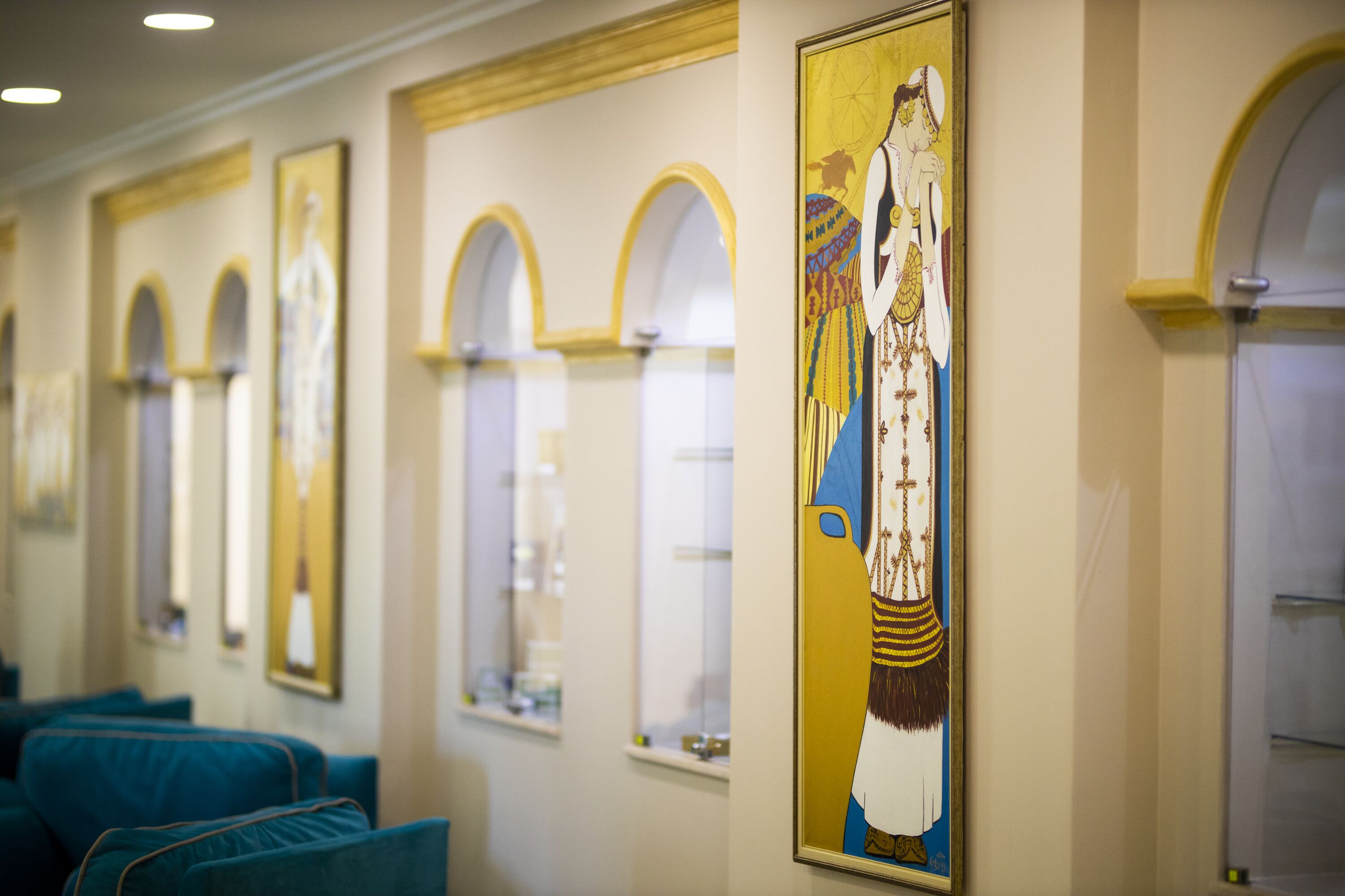 Een hotelgang met ingelijste kunst aan de muren, blauwe zitplaatsen en gewelfde ramen.