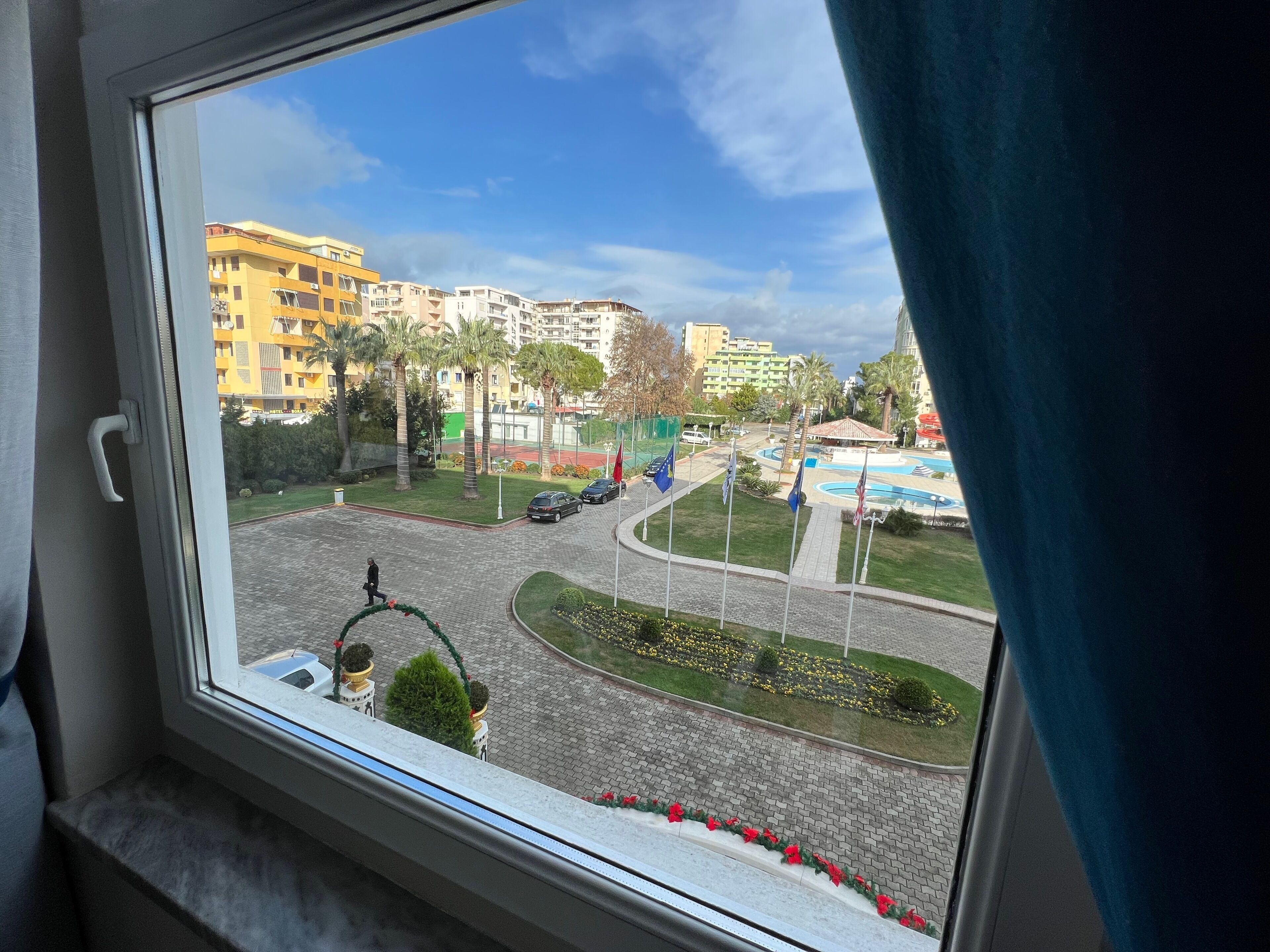A view from a window overlooking a cityscape with buildings, a roundabout, and a flag display.