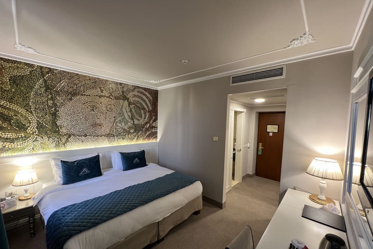 A hotel room with a large bed, a desk, a chair, a lamp, and a wall art piece.