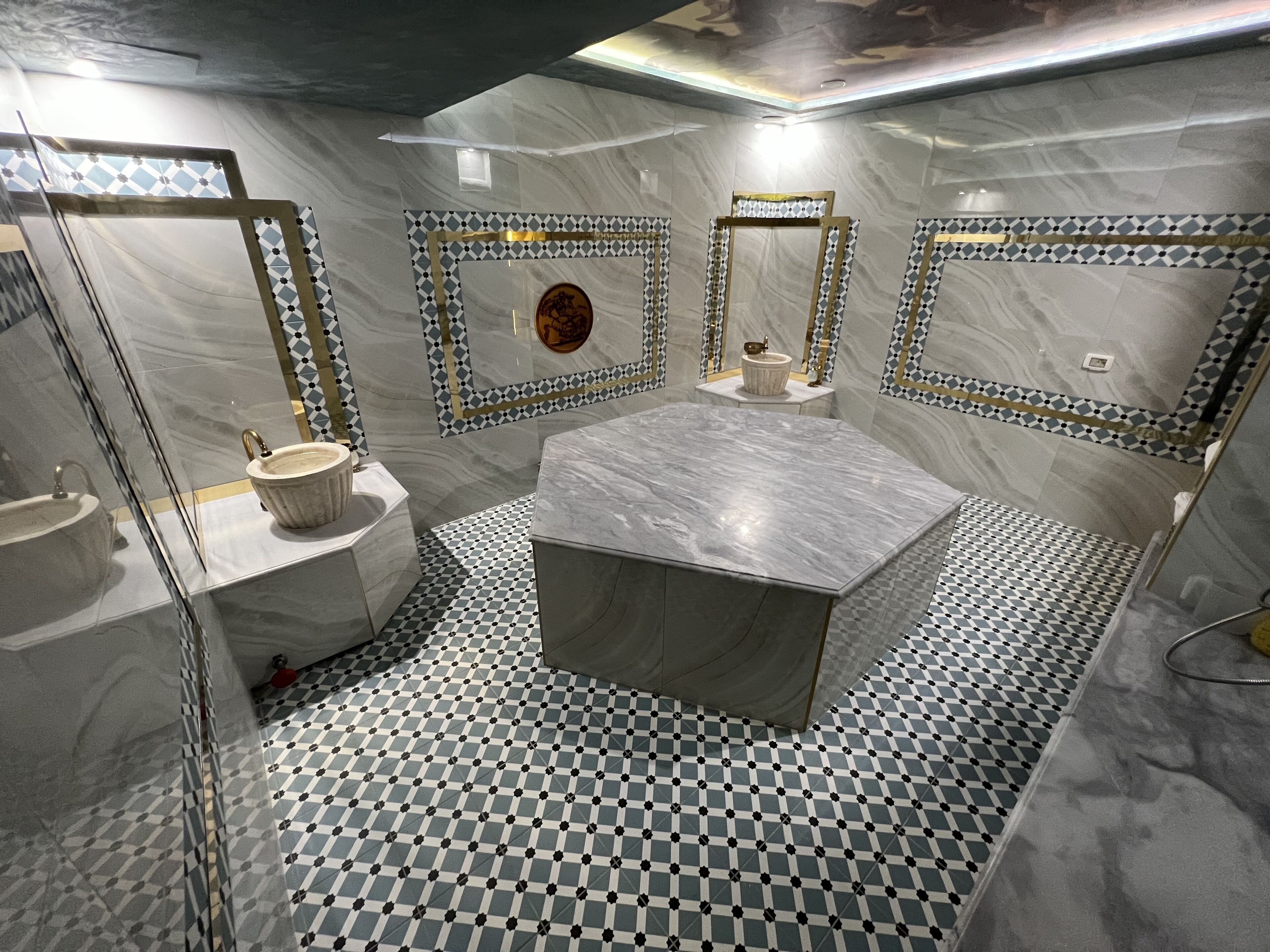 A bathroom with a checkered floor, a central marble sink, and decorative mirrors with geometric patterns.