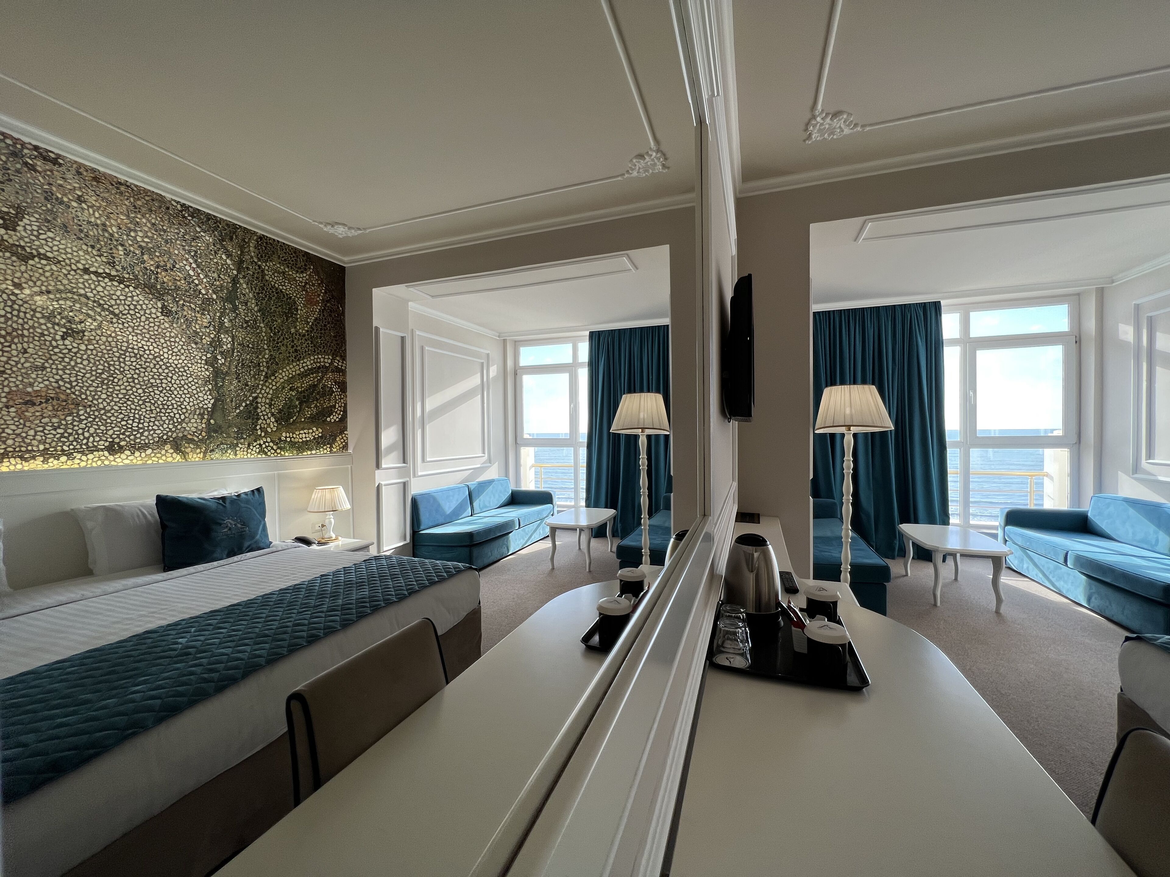 Quarto de hotel com uma cama grande, um sofá, uma escrivaninha e vista para o mar.