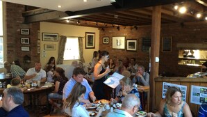A restaurant with brick walls, wooden beams, and framed pictures. Tables are set with plates, glasses, and cutlery. - The Farm Burscough (Ormskirk)