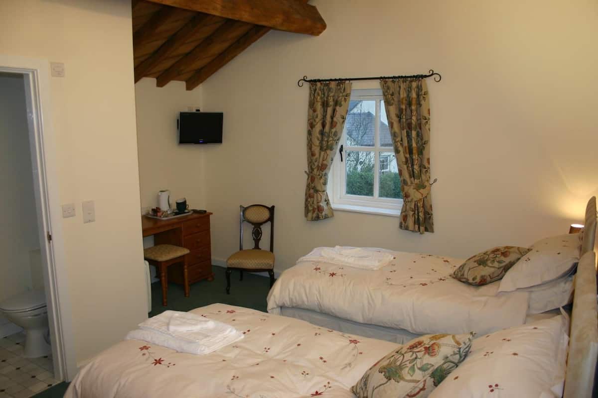A bedroom with two beds, a desk, a chair, and a television on the wall.