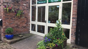 A brick building with a green sign reading "Welcome to The Farm" and a contact number. - The Farm Burscough (Ormskirk)