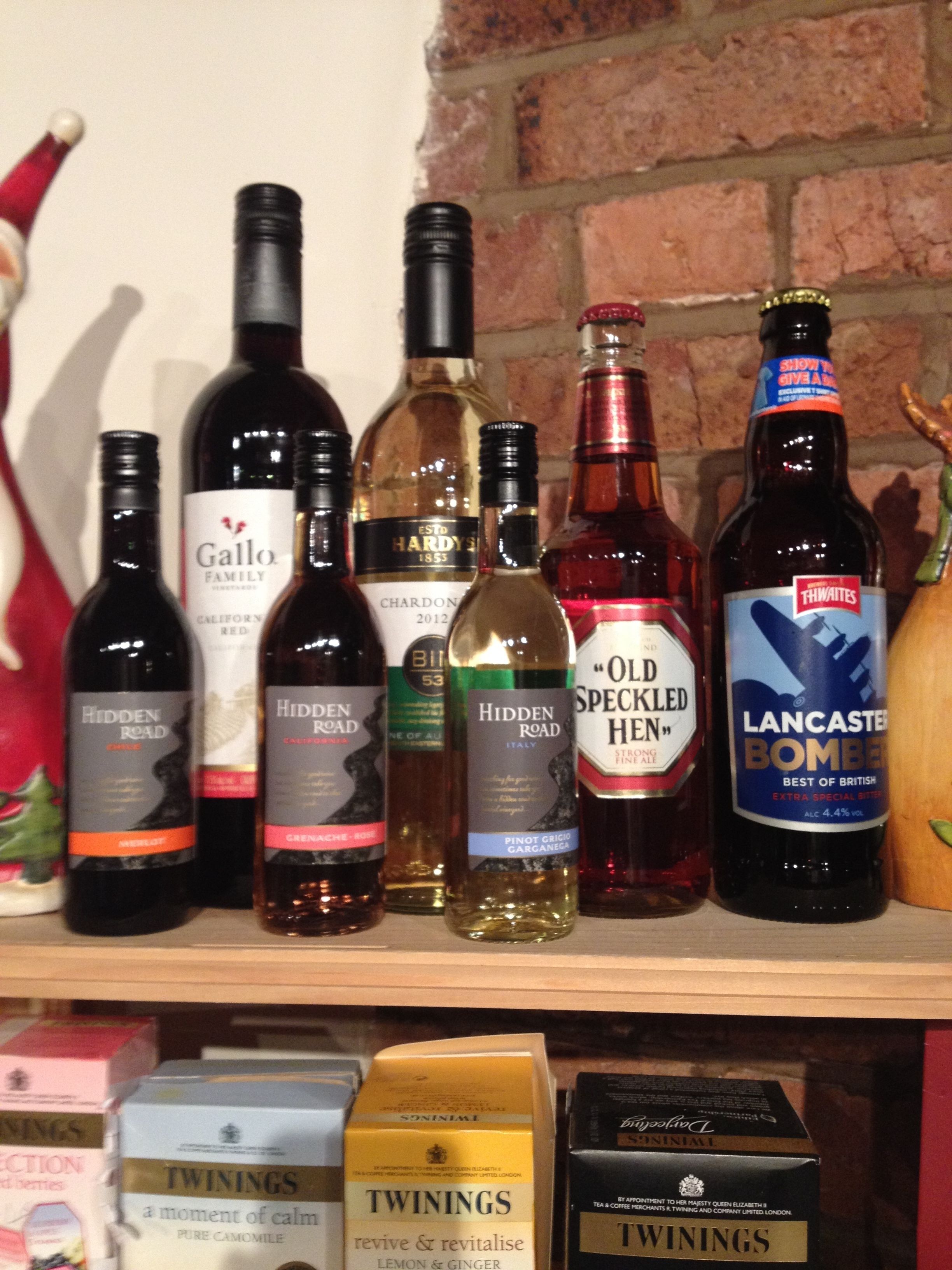 A variety of bottled beverages on a shelf, including wines and ales.