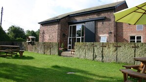 A brick building with a stone wall, a wooden picnic table, and a yellow umbrella. - The Farm Burscough (Ormskirk)