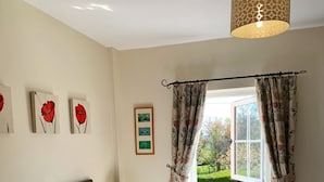 A bedroom with a bed, a nightstand, a lamp, a window with curtains, and floral artwork on the wall. - The Farm Burscough (Ormskirk)