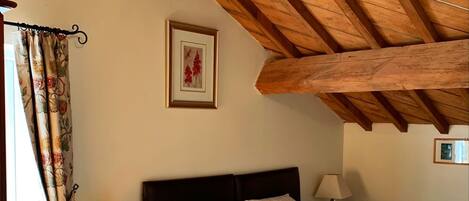 A bedroom with a wooden ceiling, a bed with white bedding, a nightstand with a lamp, and a framed picture on the wall.