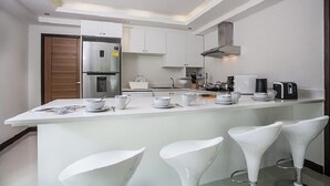 A modern kitchen with white cabinetry, a central island with bar stools, and a built-in oven. - Villa Jungle 3 Bedrooms (Kamala)