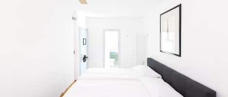A hotel room with a bed, a ceiling fan, a framed picture on the wall, and a door leading to another room.