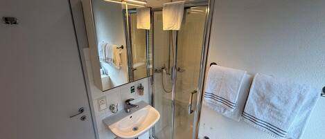 A modern bathroom with a glass-enclosed shower, a white sink, and two towels hanging on the wall.