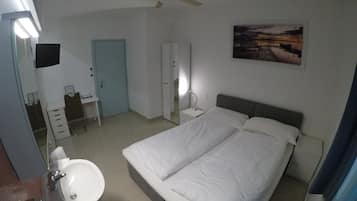 A hotel room with a bed, bedside table, lamp, and a painting on the wall.