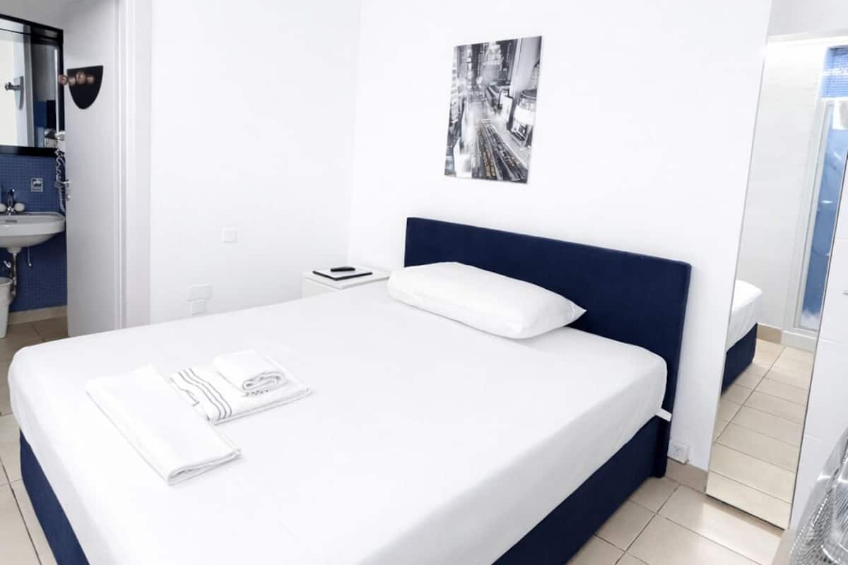 A modern hotel room with a large bed, a bathroom with a sink and mirror, and a black and white photo on the wall.