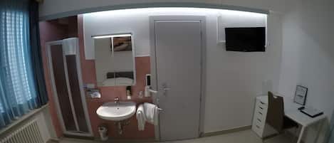 A hotel room with a bed, a bathroom with a sink, a mirror, a toilet, and a TV mounted on the wall.