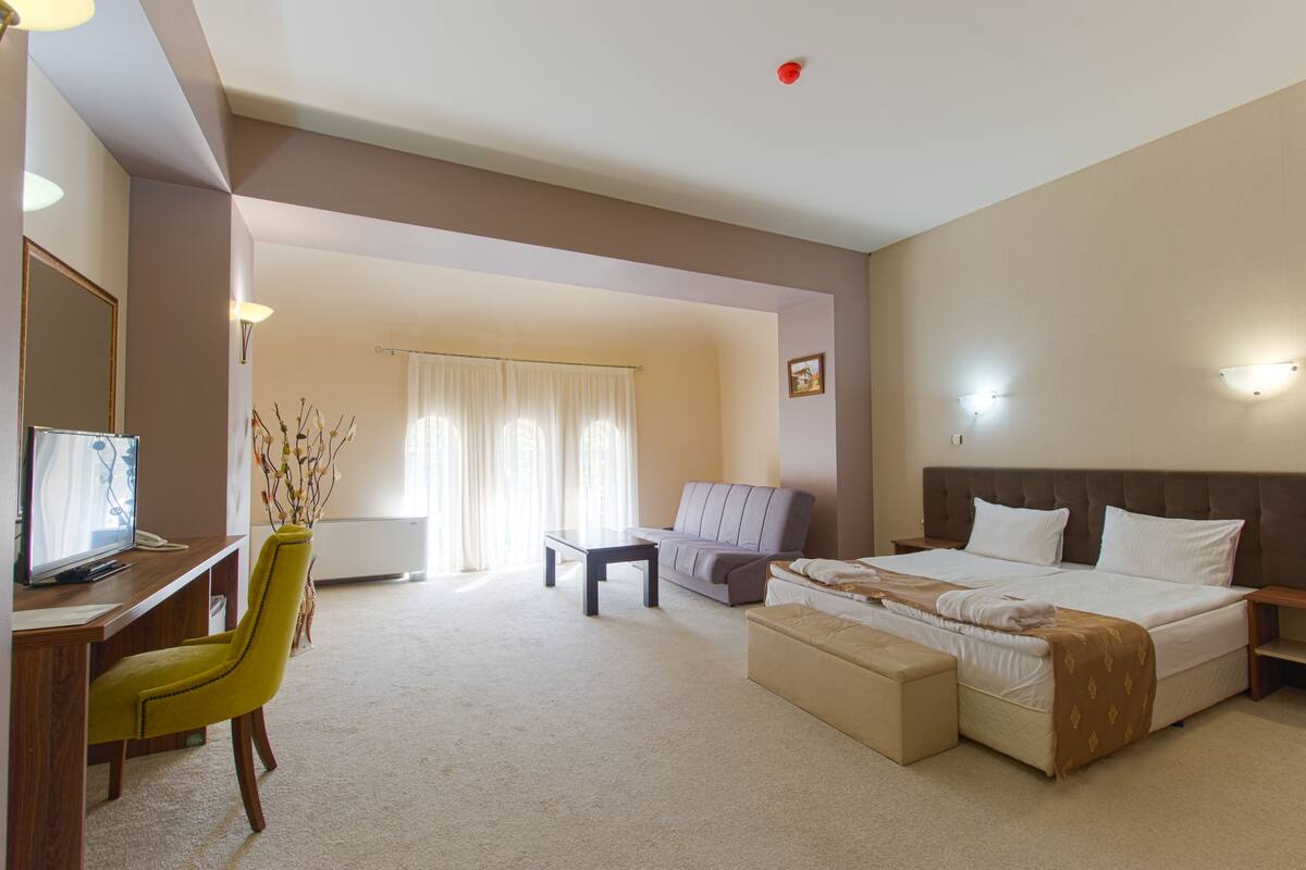 A hotel room with a bed, a desk with a computer, a chair, a sofa, and a small table.