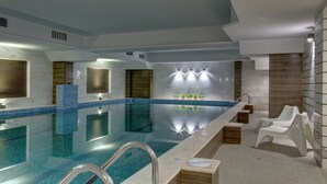 Una piscina interior moderna amb aigua cristal·lina, zona d'estar integrada i àrea de spa amb gandules.