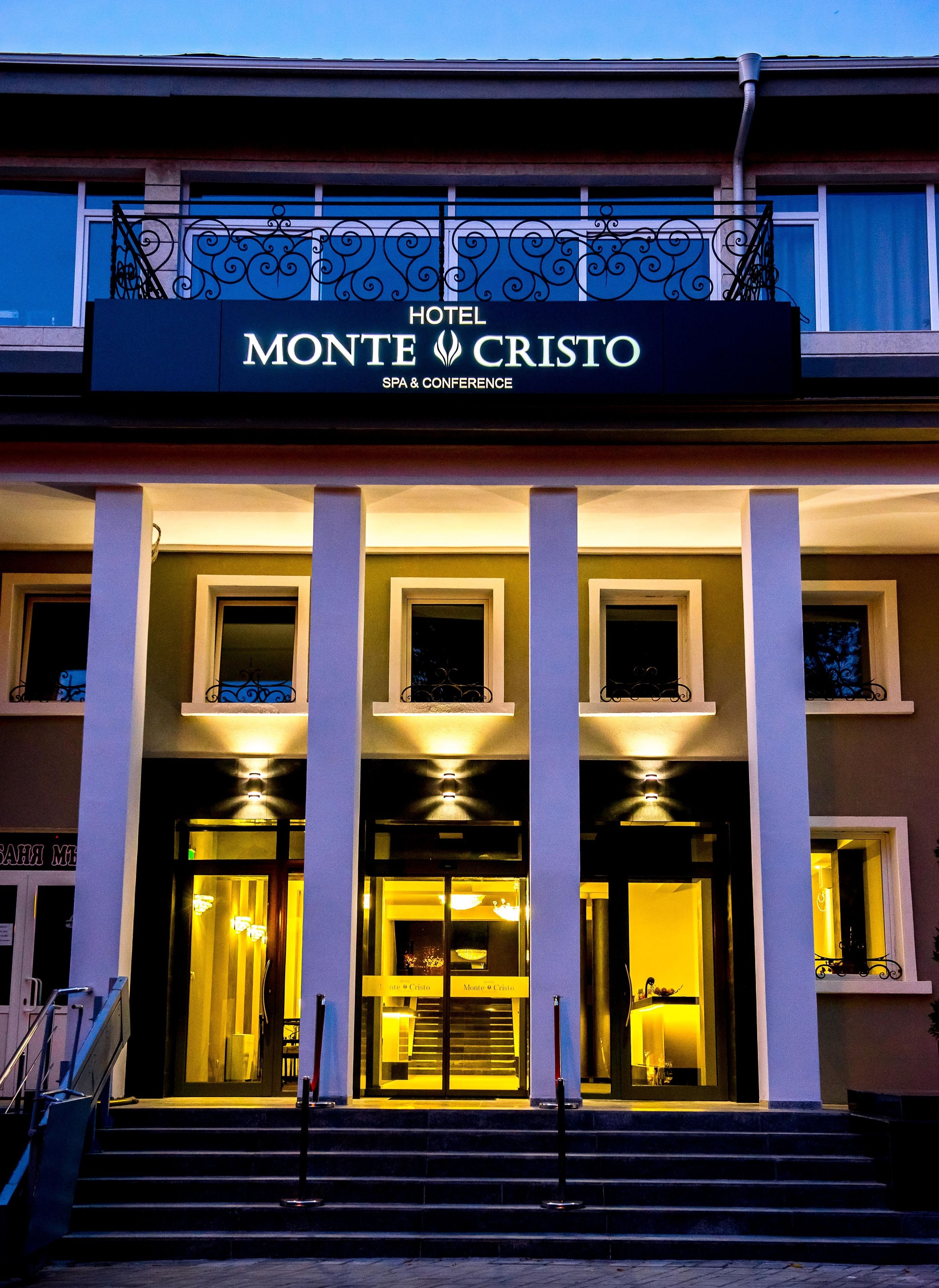 L’entrée d’un hôtel, avec une enseigne indiquant : « HÔTEL MONTE CRISTO : SPA ET CENTRE DE CONFÉRENCES ».