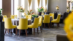 Un restaurant amb caires i taules grogues, grans finestres amb cortines i centrals florals.