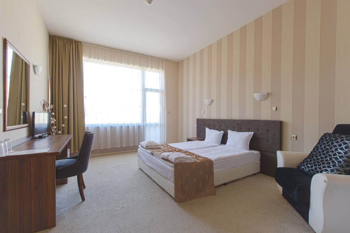 A hotel room with a large bed, a desk, a chair, and a sofa.