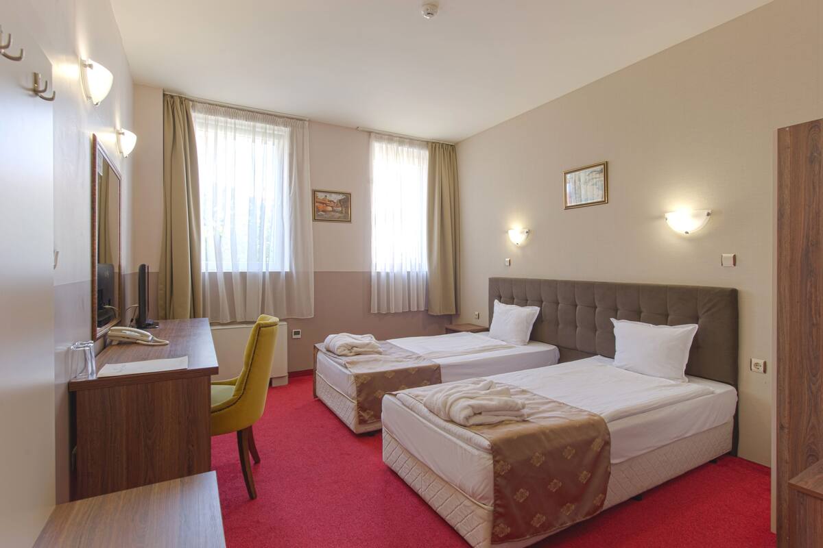 A hotel room with two beds, a desk, a chair, and a large mirror.