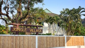 Une enseigne indiquant « Village de la jungle », avec une clôture en bambou et une végétation tropicale.