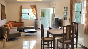 Un salon moderne avec un canapé, une table à manger et des chaises. On y trouve également un téléviseur et une fenêtre avec des rideaux.