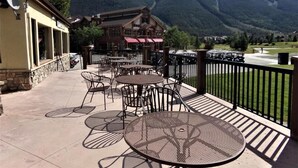 An outdoor patio with tables and chairs, a building with a red roof, and a mountainous backdrop.