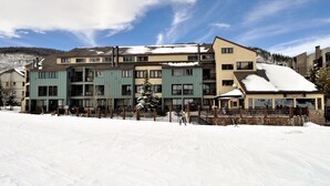 A multi-story hotel with a snow-covered roof, a ski lift, and a mountain backdrop.