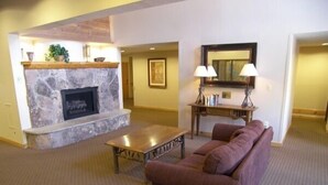 A living room with a stone fireplace, a wooden coffee table, a purple sofa, and a desk with lamps.