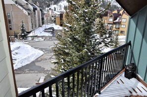 Un balcon donnant sur une rue enneigée, des immeubles et un arbre recouvert de neige.