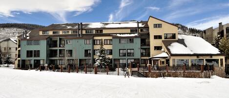 A multi-story hotel with a snow-covered roof, a ski lift, and a mountain backdrop.