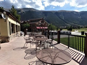 Une terrasse extérieure avec des tables et des chaises, un bâtiment avec un toit rouge et un paysage montagneux en arrière-plan.