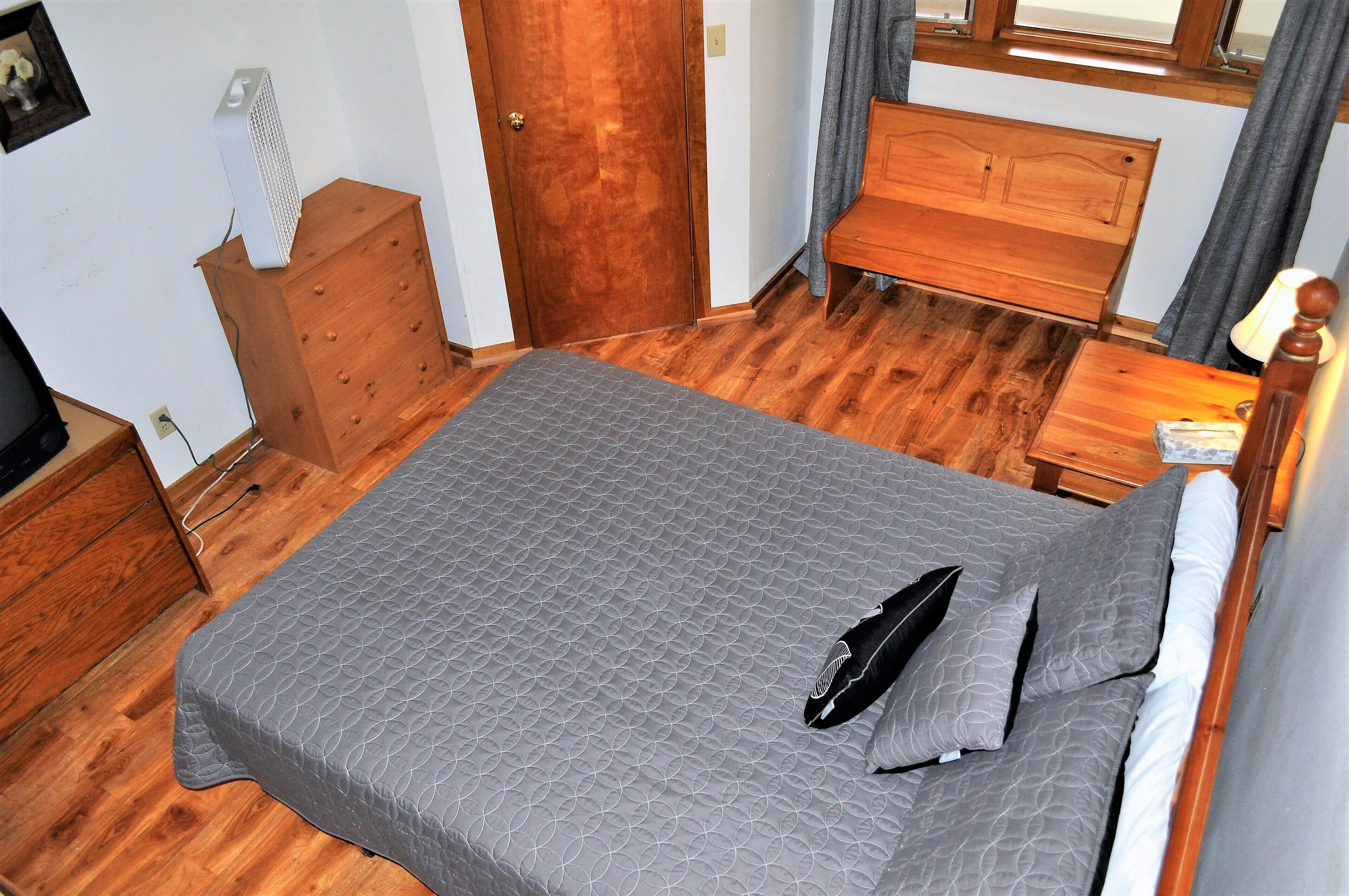 Ein Schlafzimmer mit einem hölzernen Bett, einem Schminktisch, einem Nachttisch und einem Fenster mit Vorhängen.