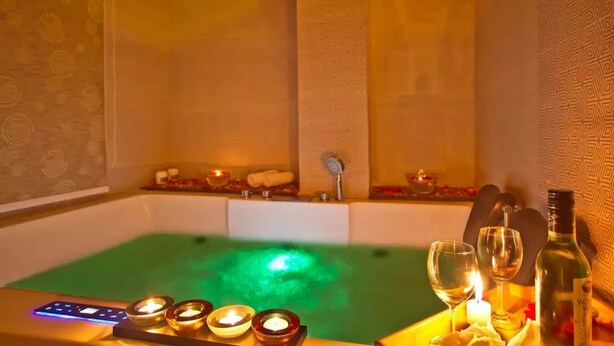 Un baño de spa con luz verde, velas y una botella de vino.