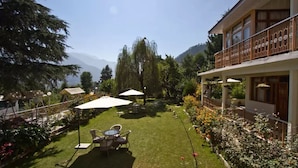 Un hotel con balcón, césped con mesa y sillas, y vistas a las montañas.