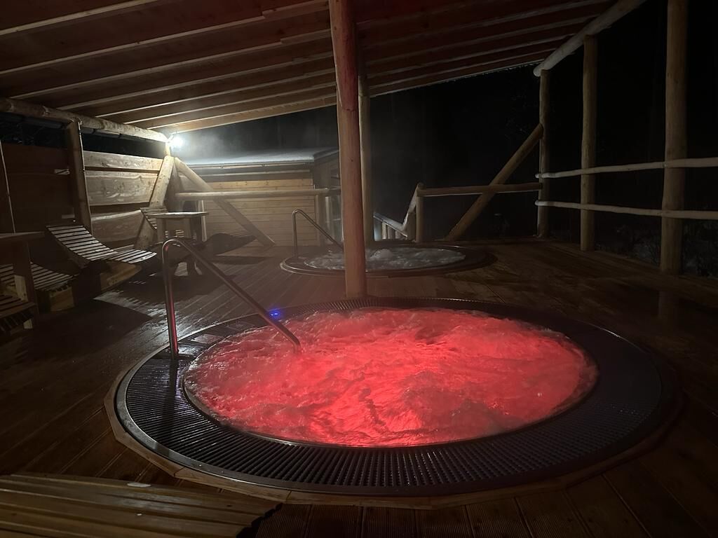 Un jacuzzi con cubierta de madera y estructura metálica, rodeado de barandillas de madera y techo de madera.
