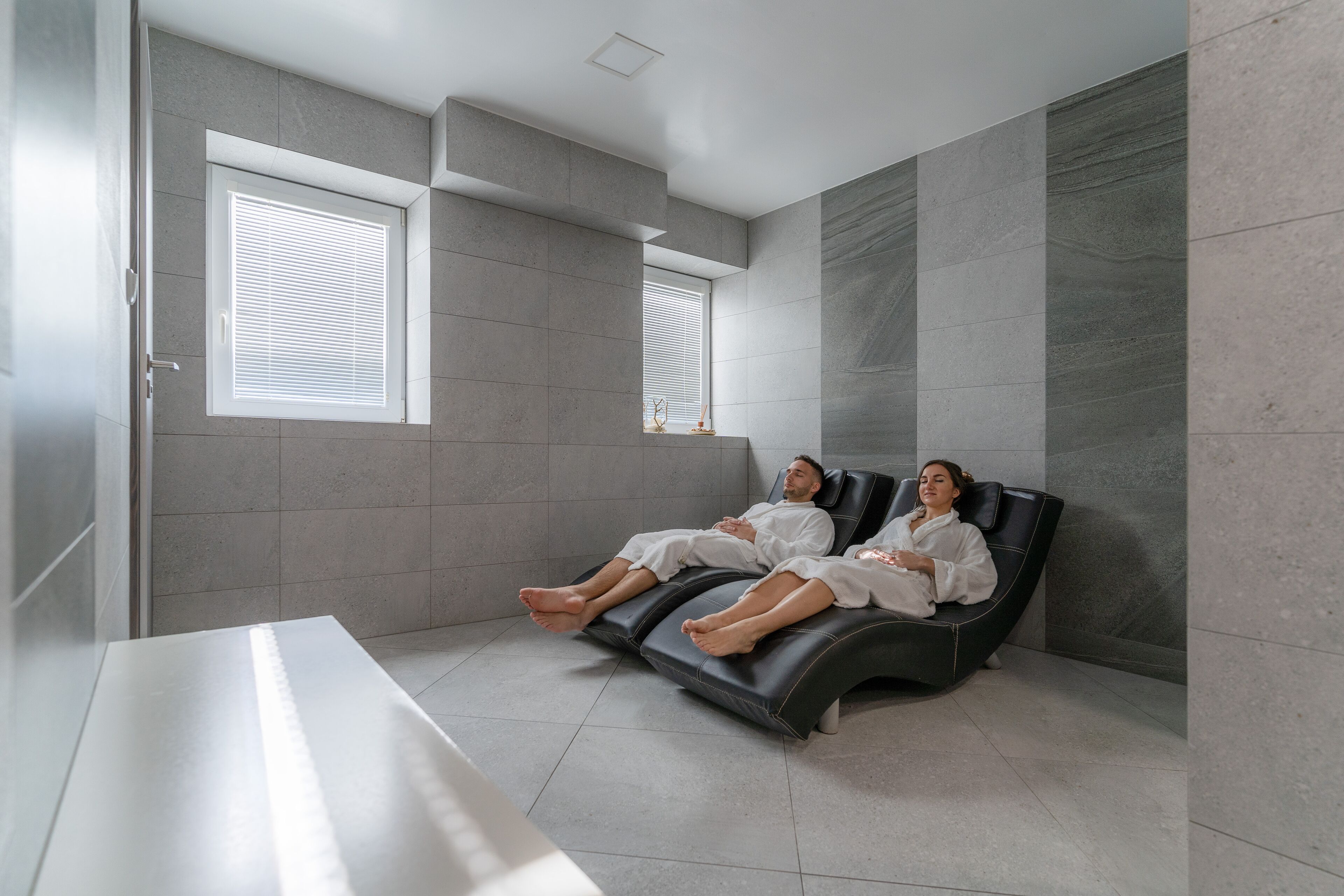 A modern spa room with two reclining chairs, a large window, and a white reception desk.